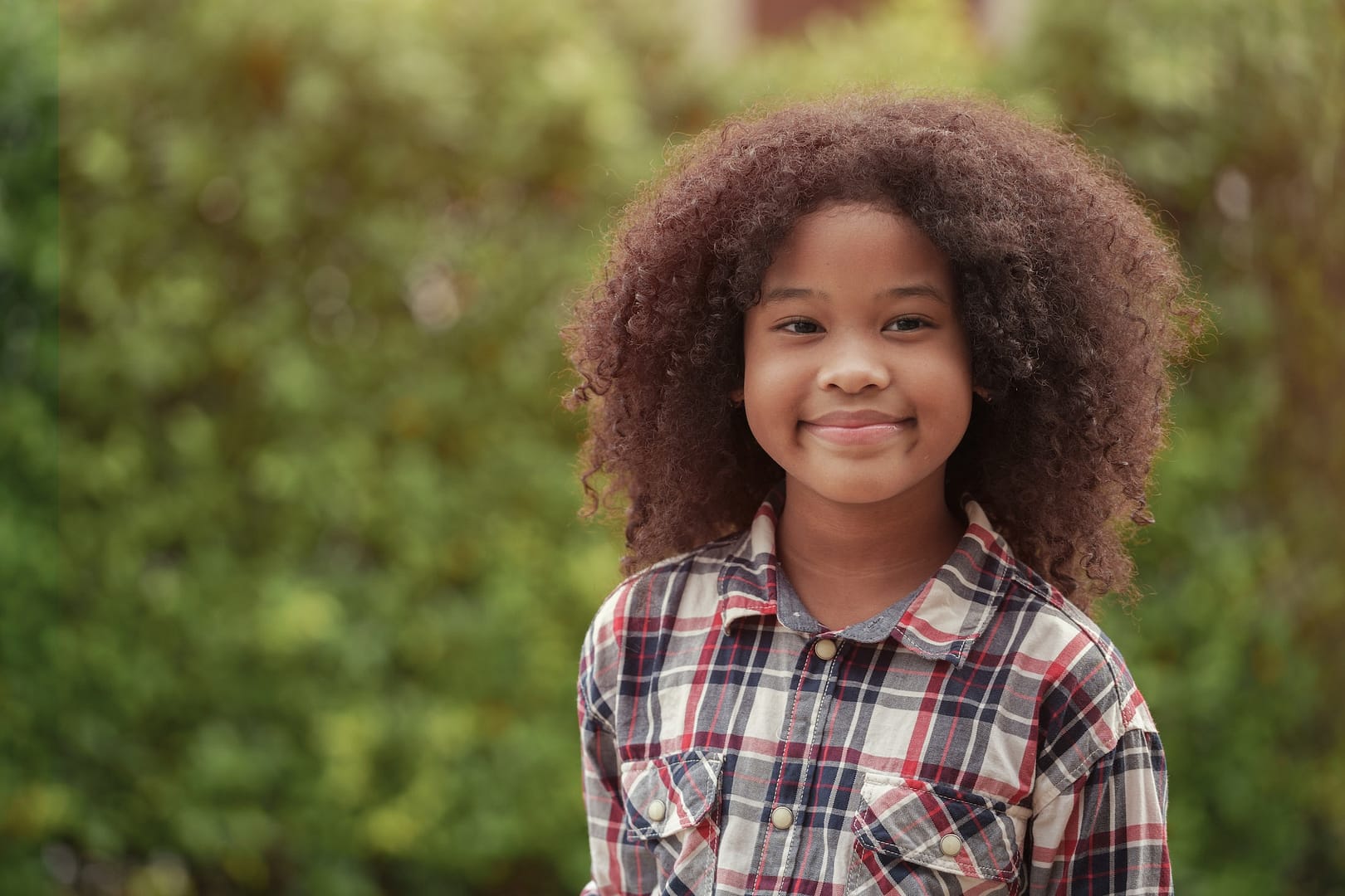 African American kid girl is smiling in the garden or outdoors.